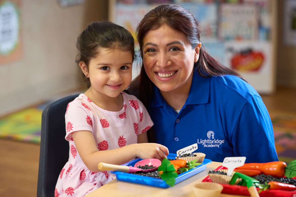 A teacher posing with a student while they are learning about types of food
